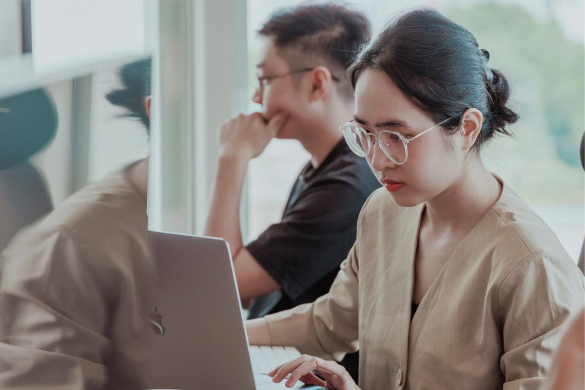 A Zühlke colleague working on a laptop in the office while another colleague collaborates nearby, illustrating a focused and supportive work environment.