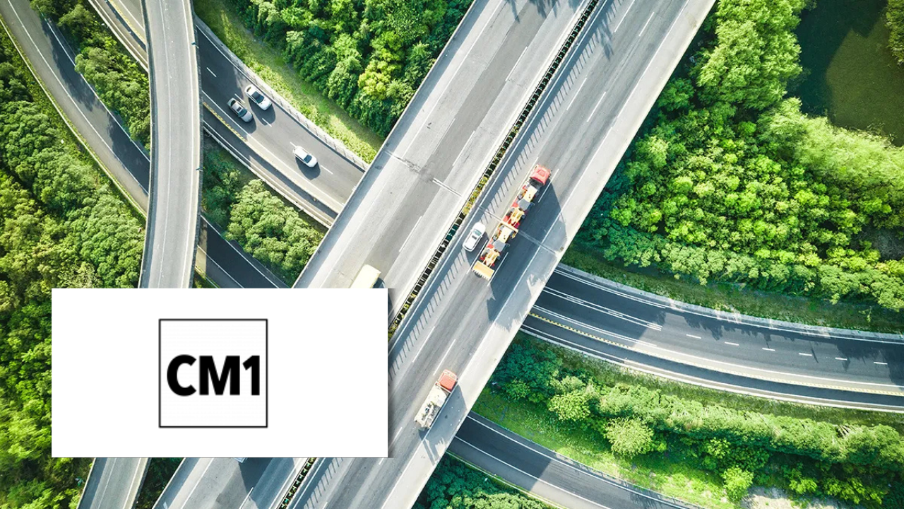 Aerial view of highway overpasses surrounded by green trees, with construction vehicles on the road, next to the CM1 logo.