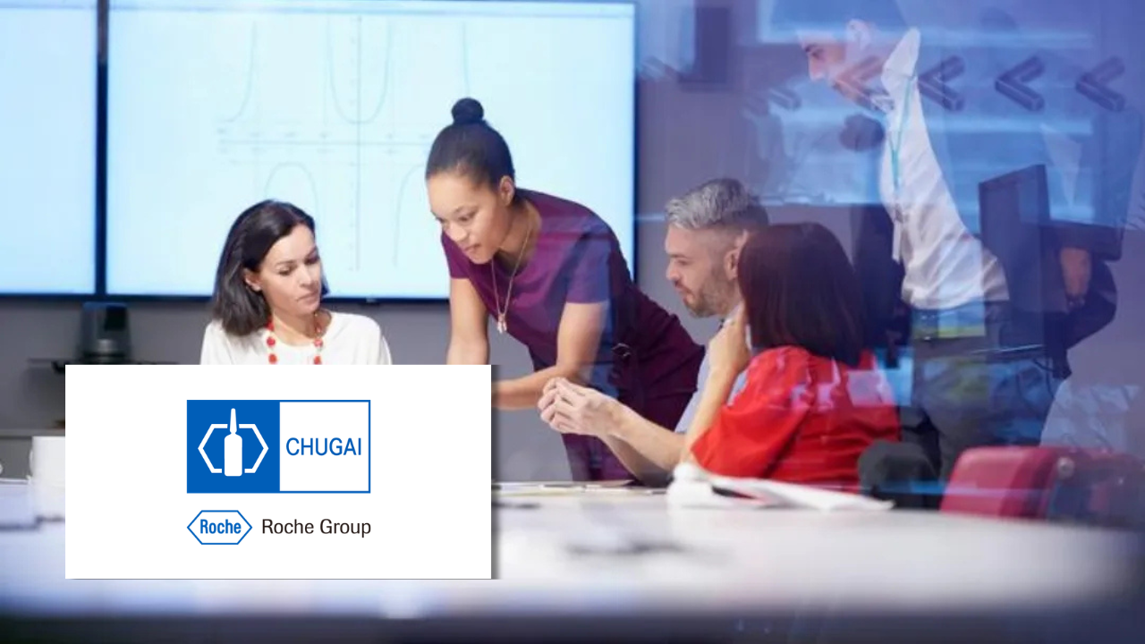 Colleagues collaborating around a table with data charts displayed on screens behind them, next to the Chugai and Roche Group logos.