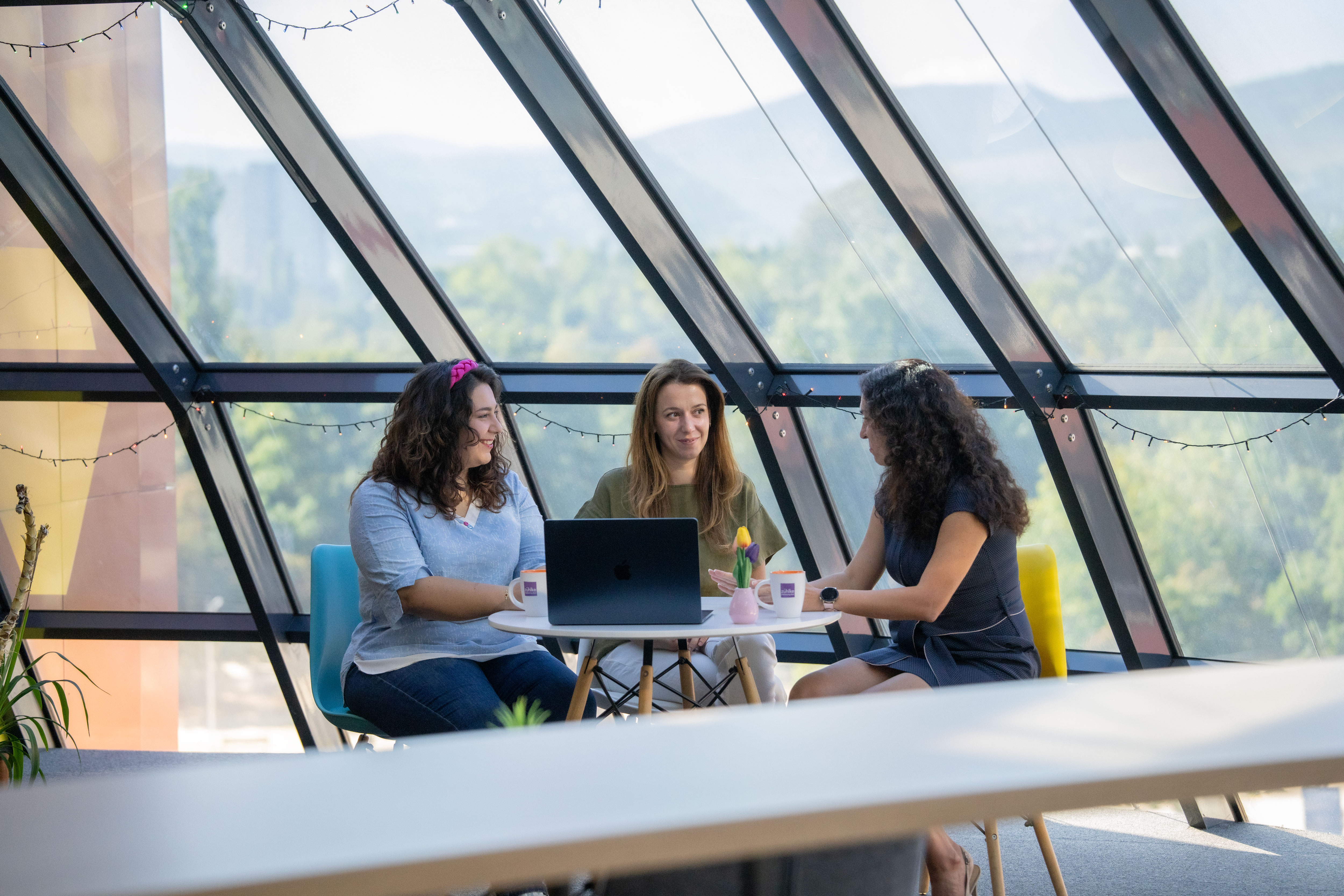 Three colleagues sitting together, smiling as they review content on a laptop during a collaborative work session.