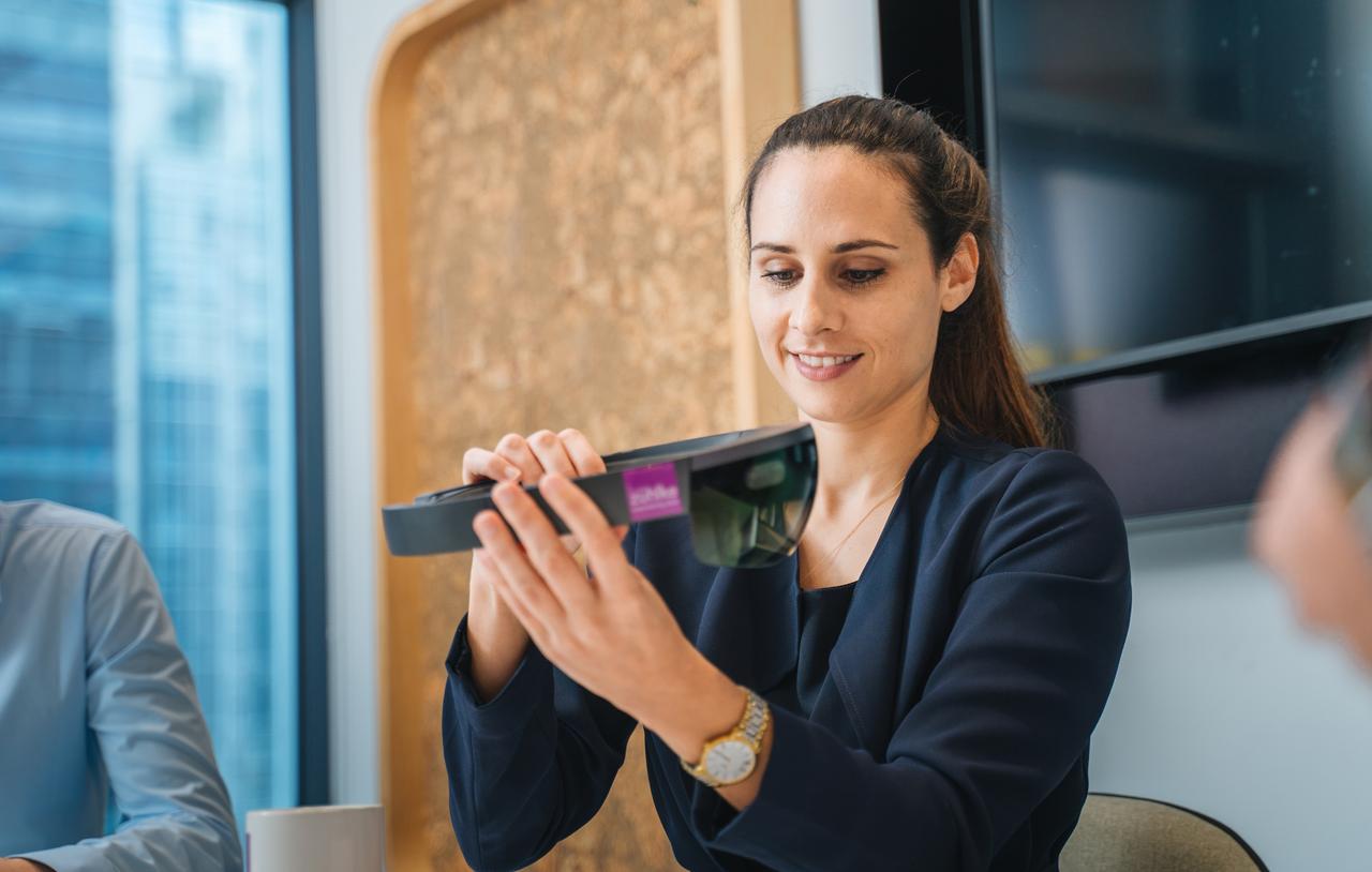 A woman professional in an office setting holding a VR headset in hands and smiling