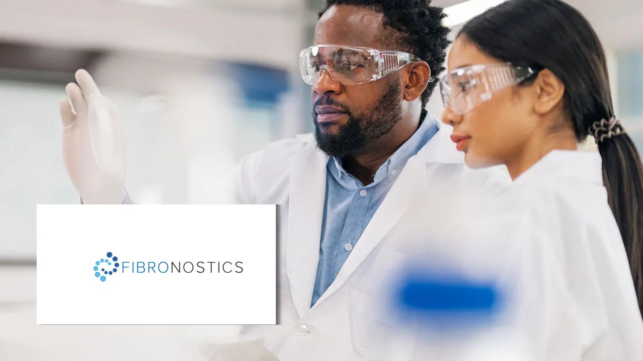 Two lab researchers in white coats and safety goggles examining a sample together, next to the Fibronostics logo.