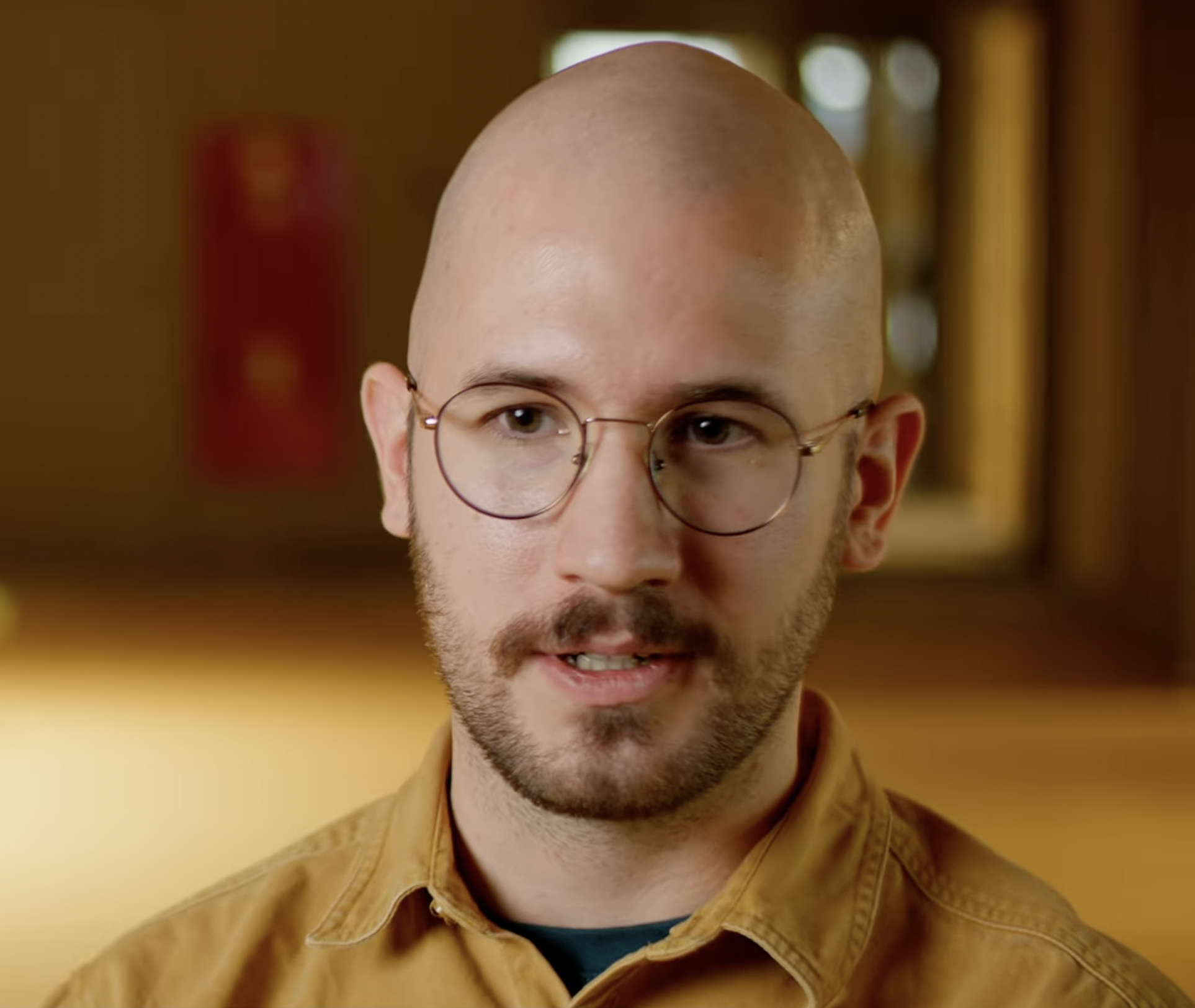 A man in round glassess sitting in a soft yellow office open space room