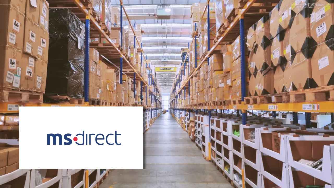 Interior of a large warehouse with tall shelving units stacked with boxed inventory, next to the ms direct logo.
