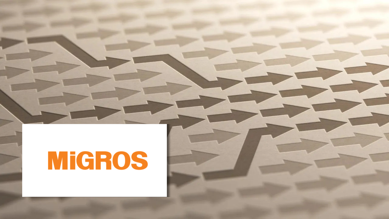 Close-up of overlapping arrow patterns etched into a metallic surface, next to the Migros logo.