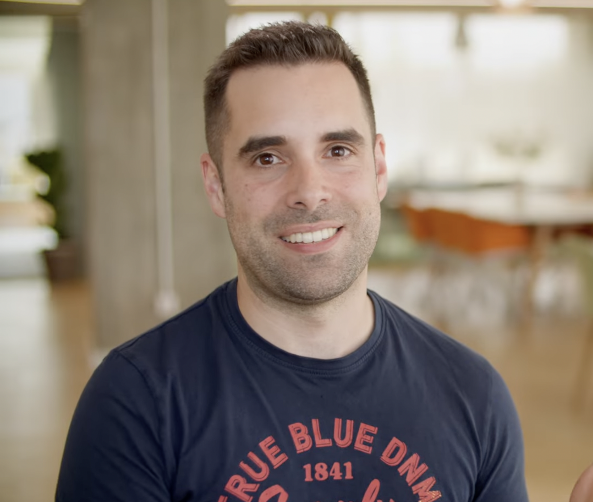 A man sitting on a chair in the light open office setting and smiling