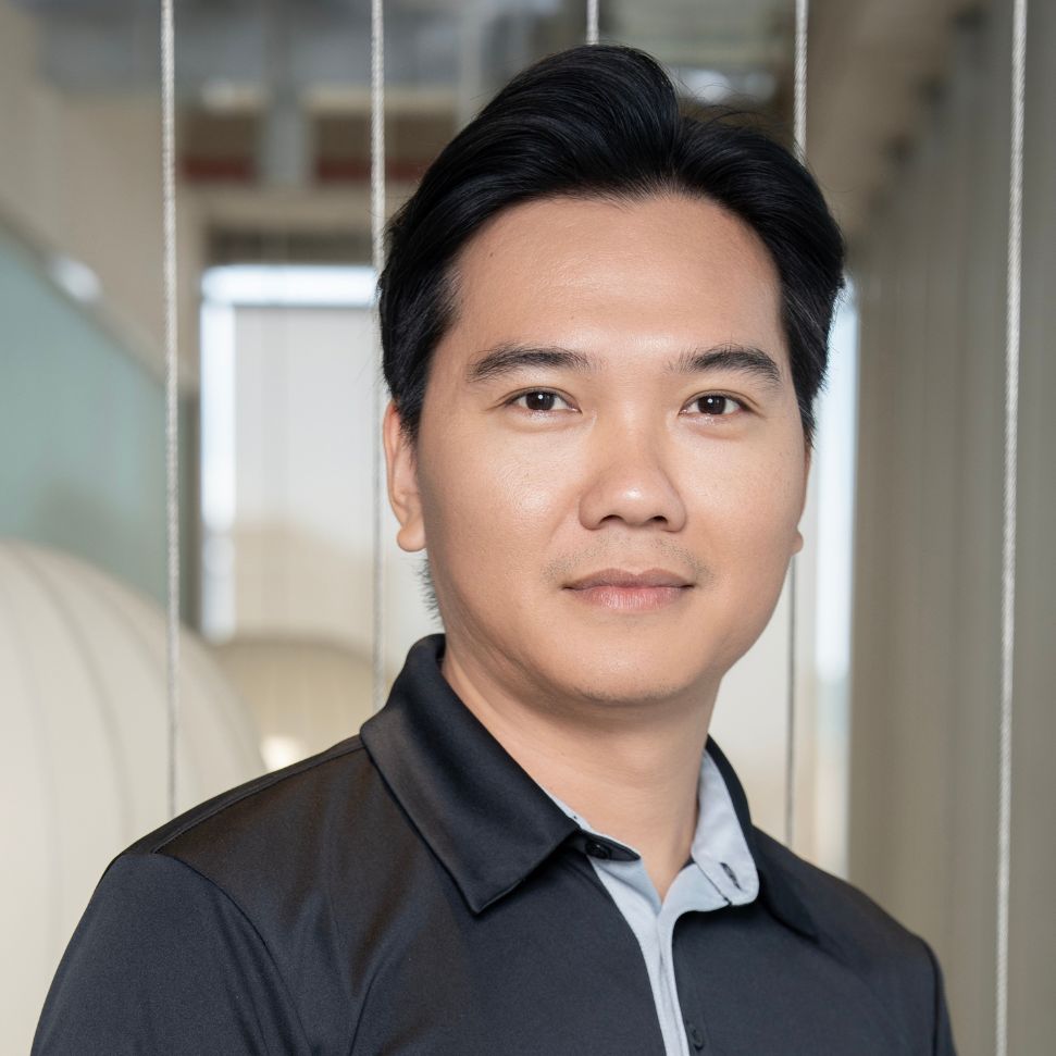 Portrait of a man standing in a modern office, looking at the camera with a neutral expression.