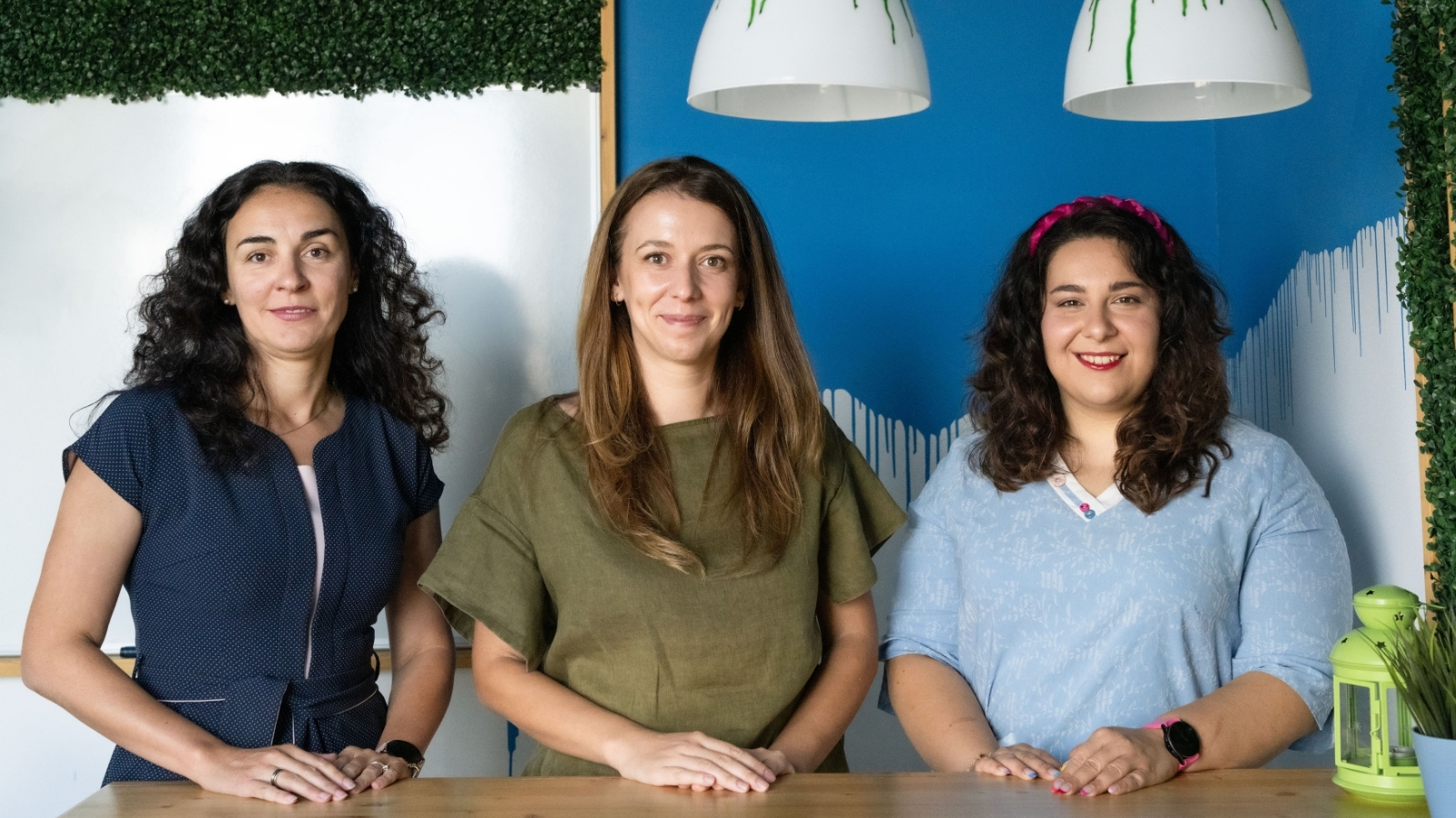 Portrait of three women standing together and smiling in a modern office environment.
