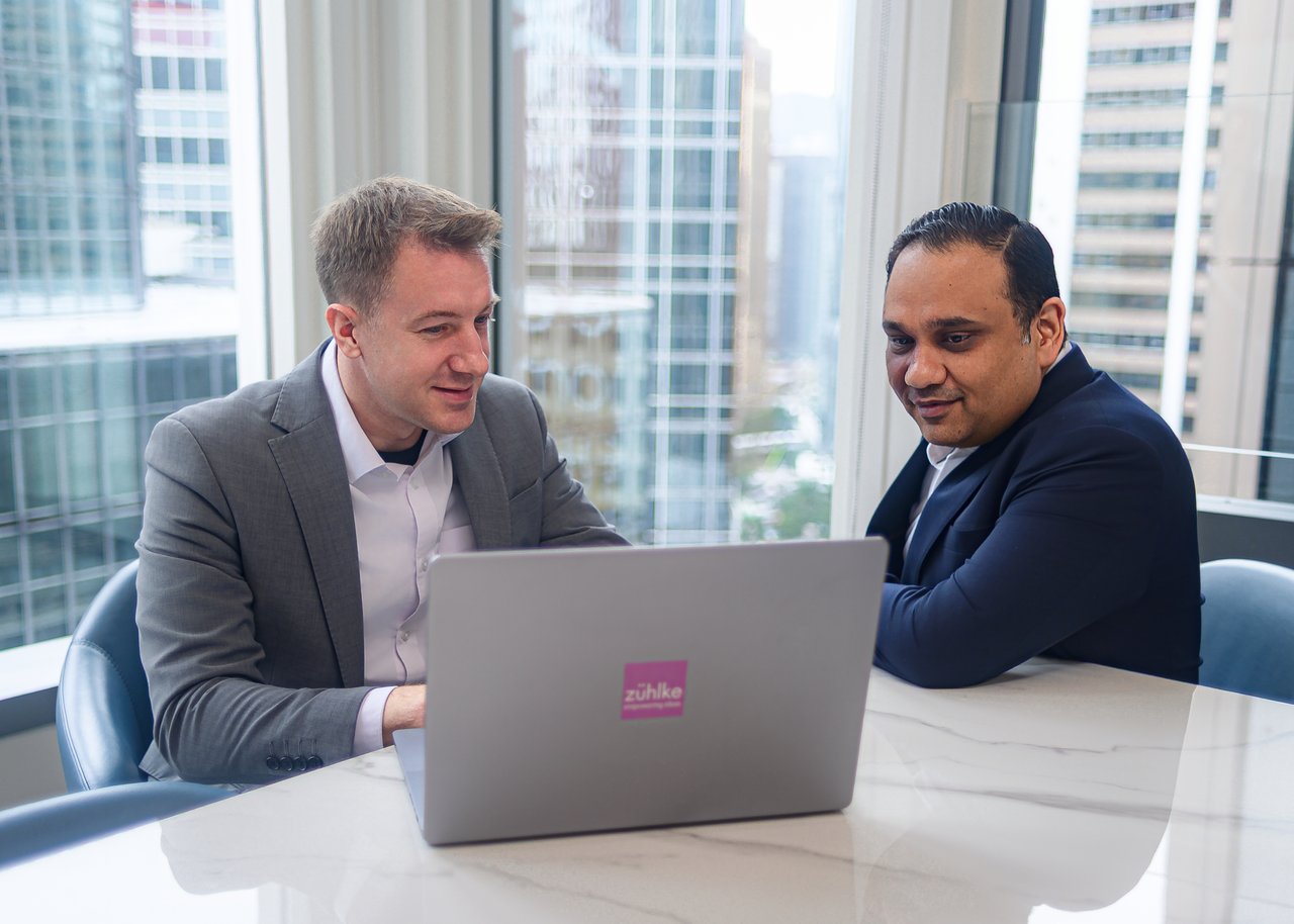 Two men colleagues sitting at the office desk in front of the laptop, with the skyscraper buildings panorama in the background