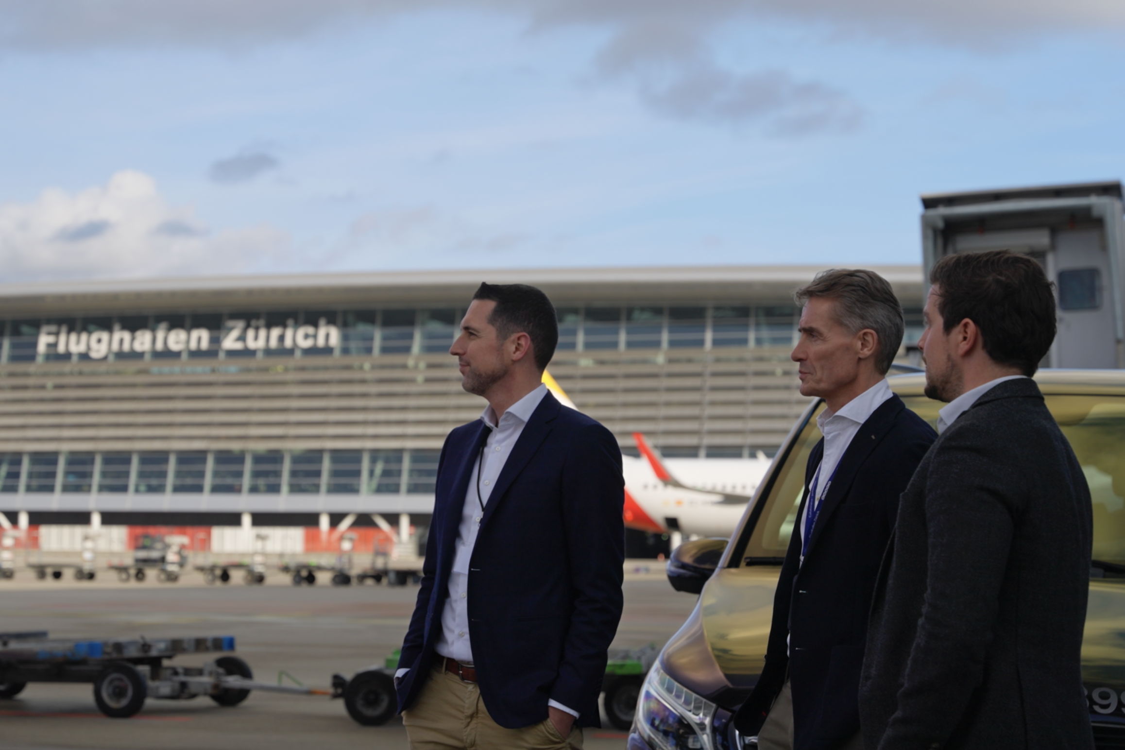 Three men standing in front of Zurich Airport and looking into distance