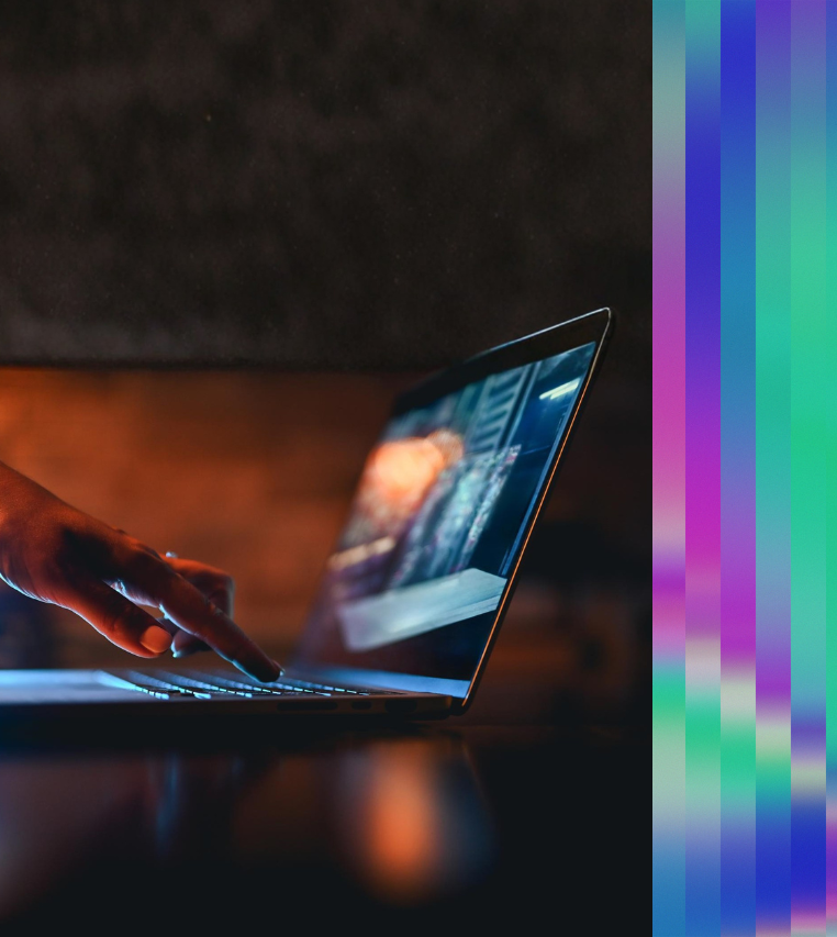 Close-up of a hand typing on a laptop keyboard, with a glowing screen in a low-light setting.
