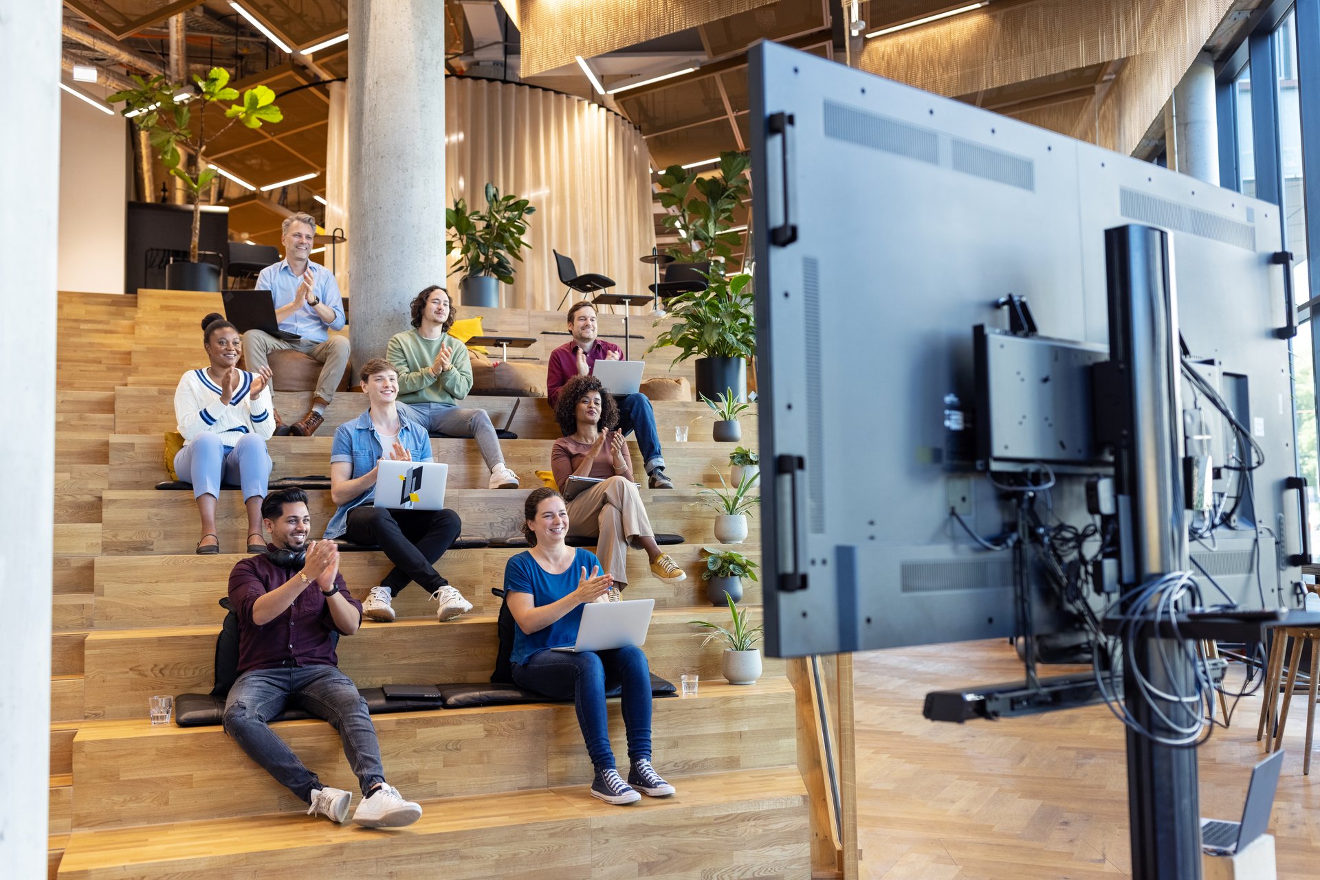 Business professionals sitting on steps and applauding after a successful online meeting at creative office.